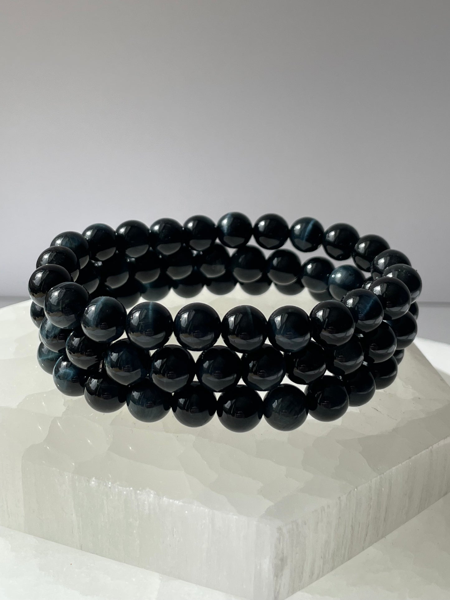Blue Tiger Eye healing bracelet on a white quartz crystal background.