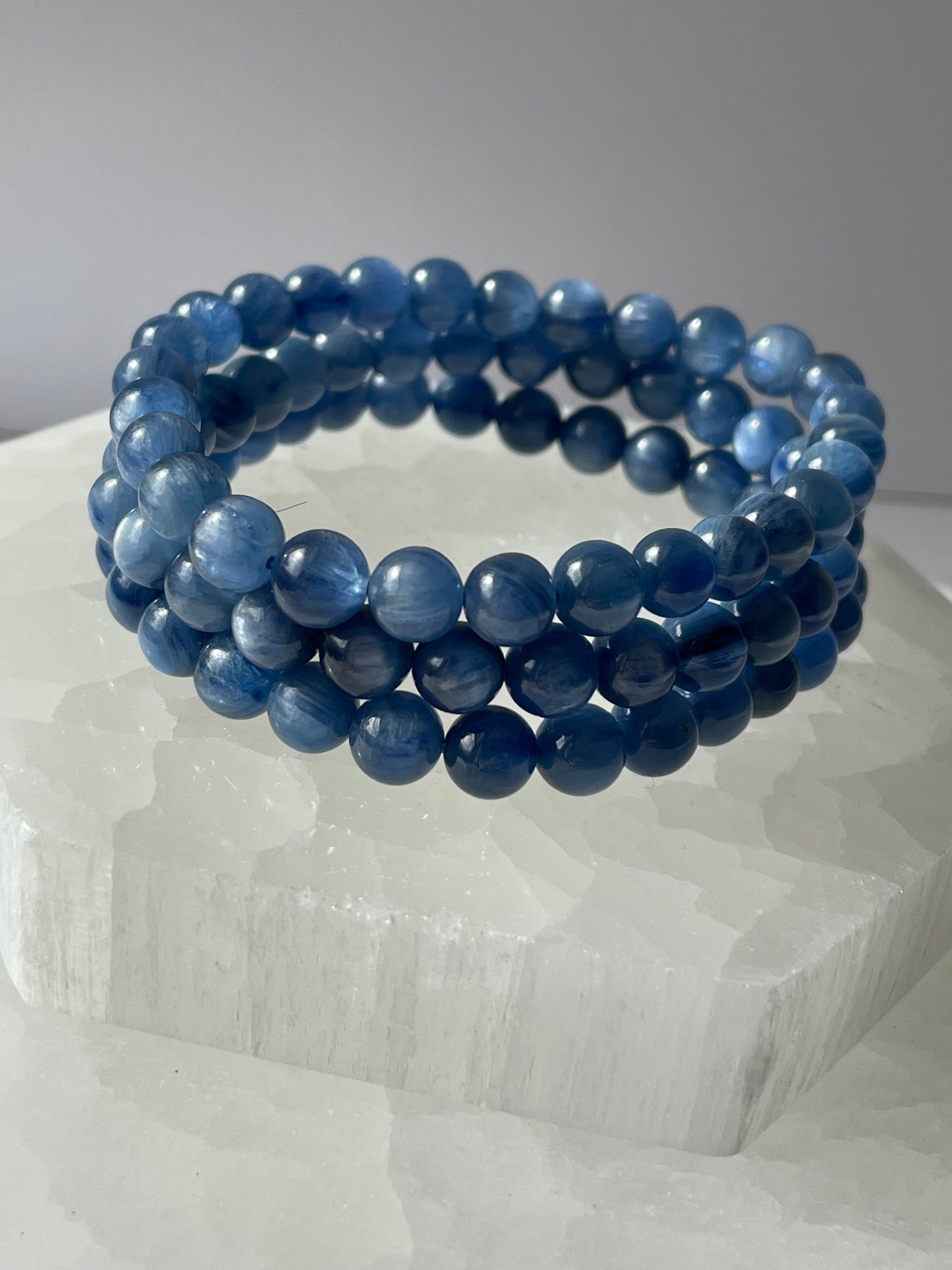 A delicate 7-inch Blue Kyanite bracelet with smooth 6 mm beads resting on a white crystal.