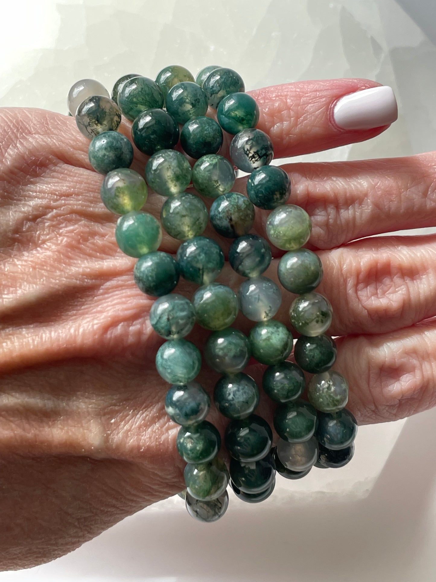 Green moss agate bracelet of 8mm beads displayed on girl’s finger root.