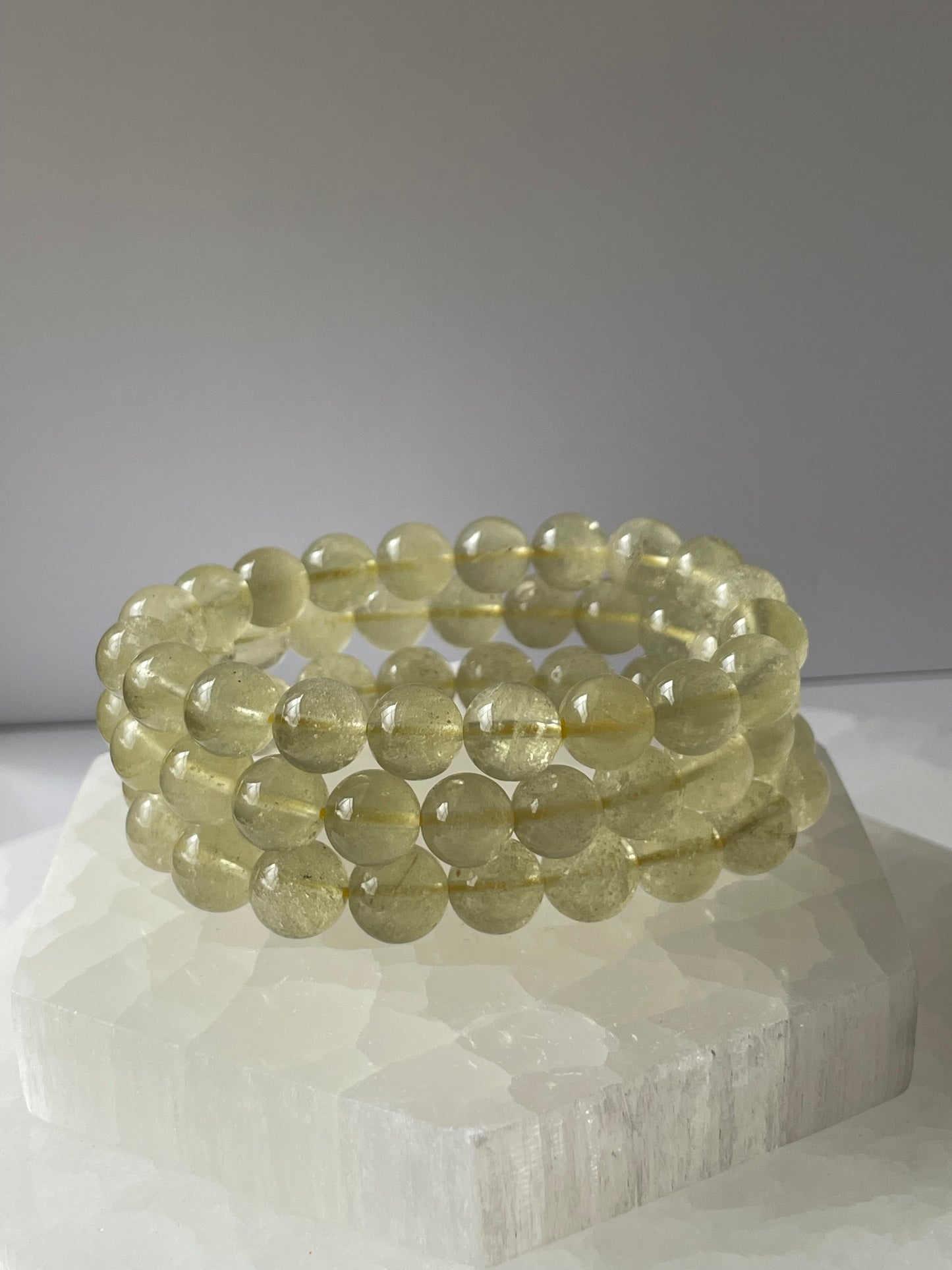 Yellow crystal Libyan Desert Glass bracelet displayed over a white crystal base.