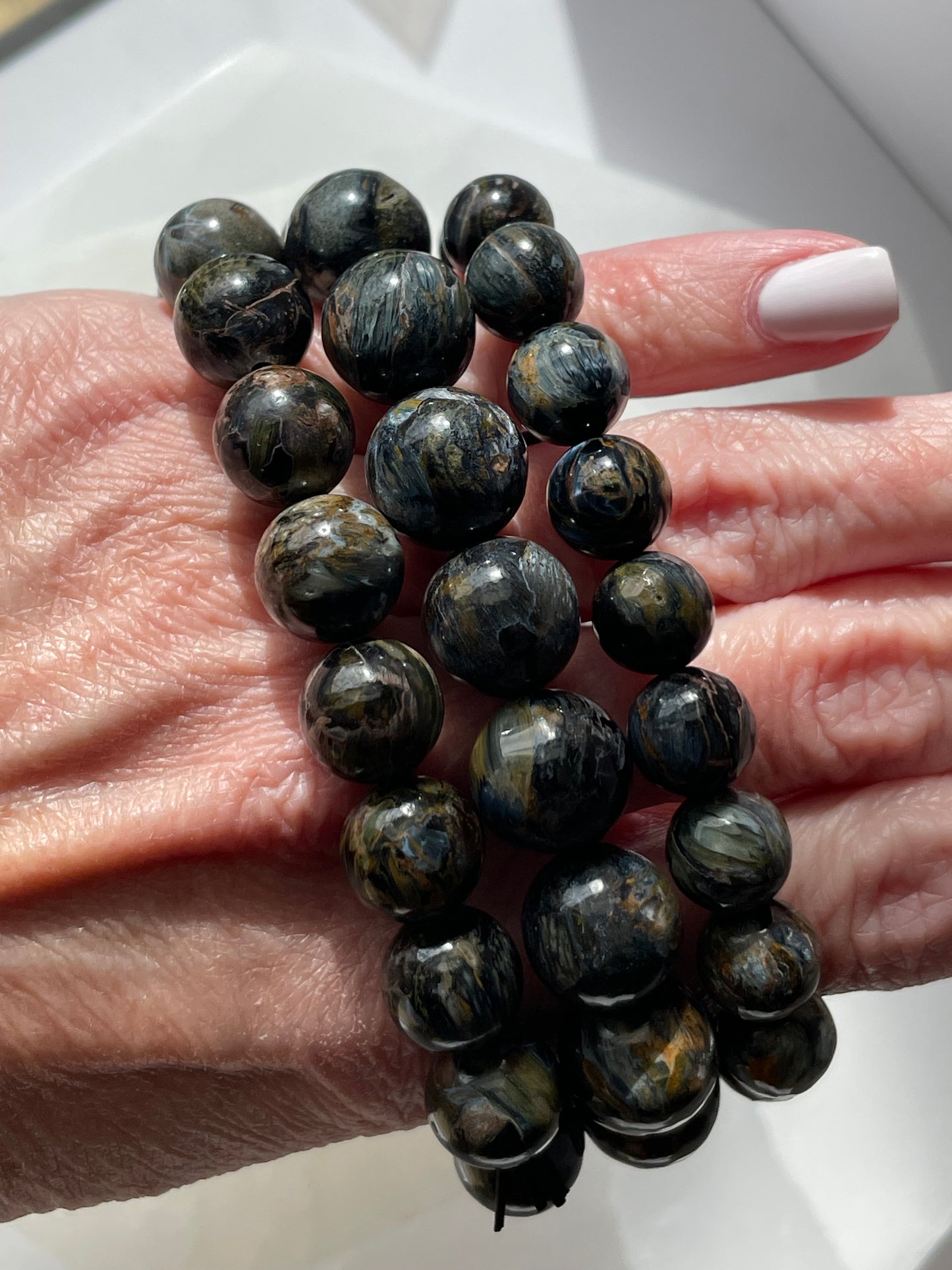 A Blue Pietersite bead bracelet worn and displayed on female knuckles.