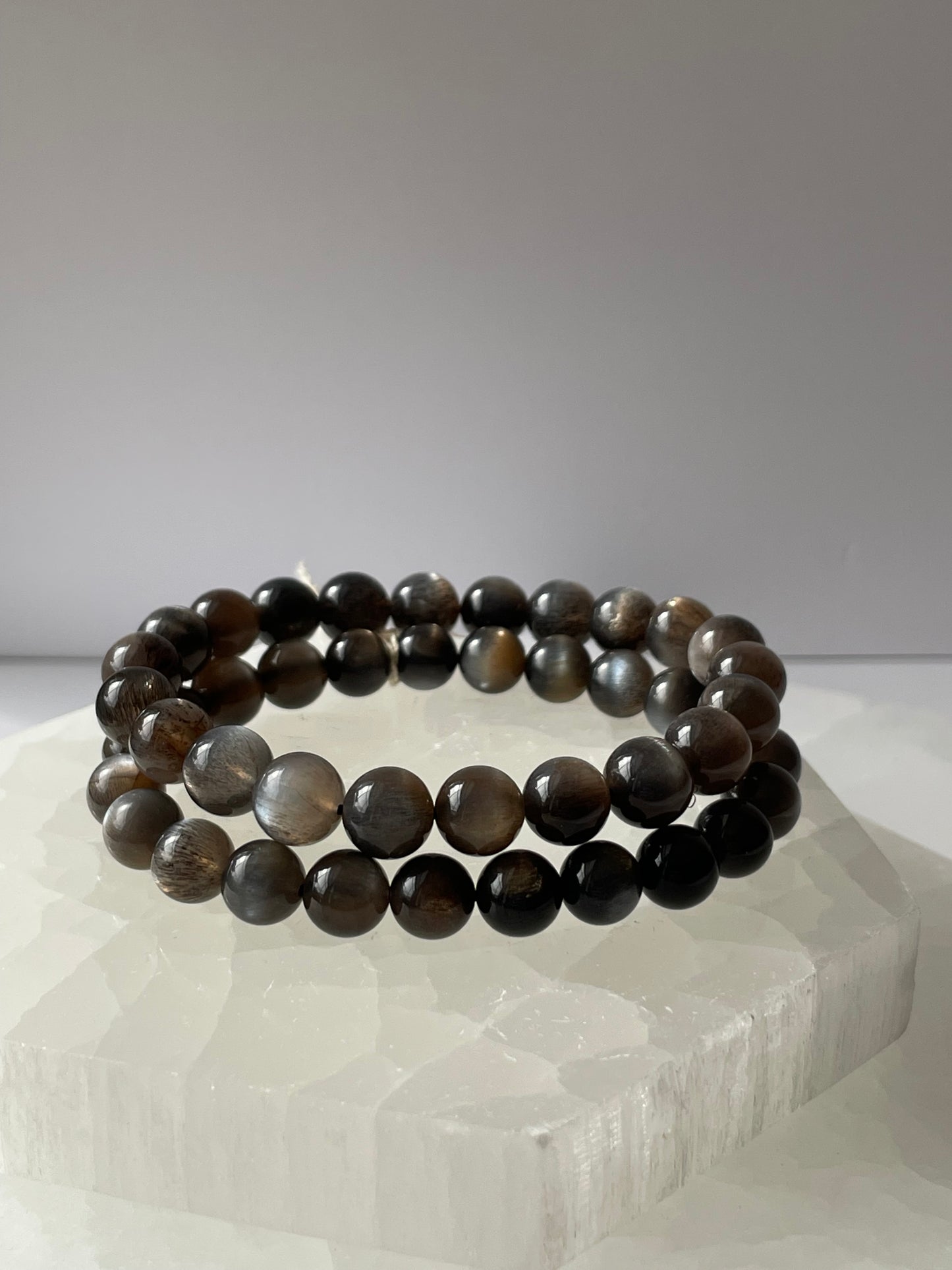 A black moonstone bracelet with 8 mm beads, displayed on a white surface.