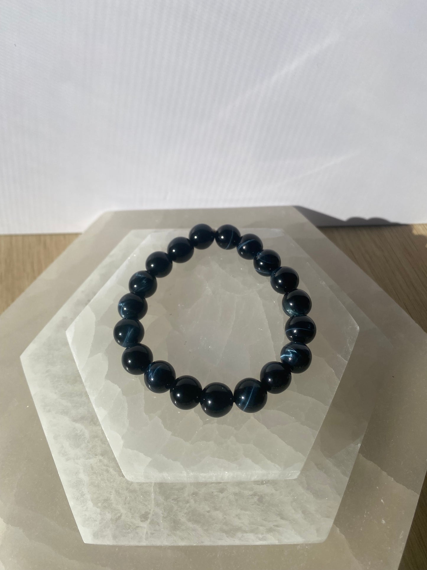 Blue Tiger Eye bracelet arranged on a modern white display base.