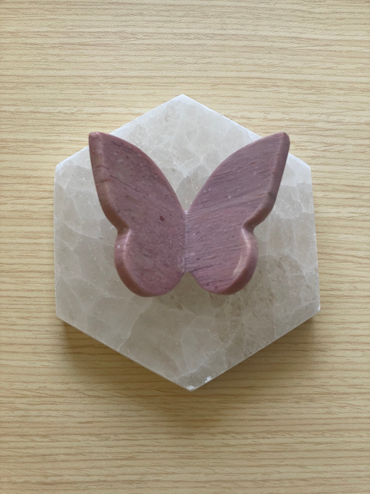 A butterfly carving made of pink petrified wood placed on a hexagonal stone.