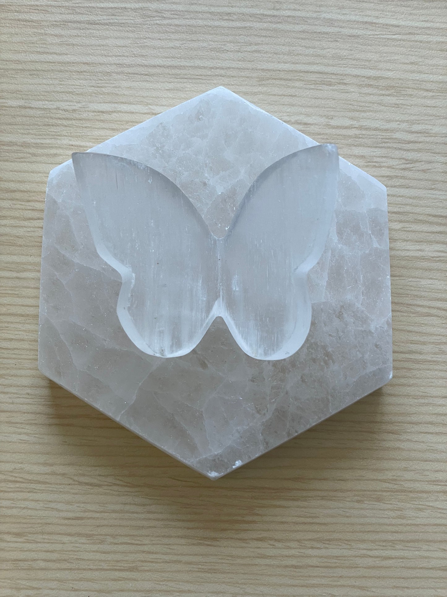 Selenite butterfly carving on hexagonal stone over wood surface