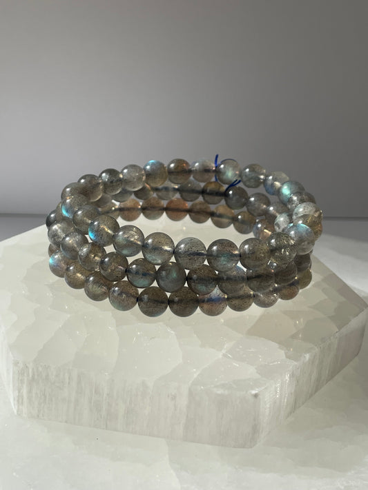 Labradorite bracelet with round beads displayed on a white crystal.
