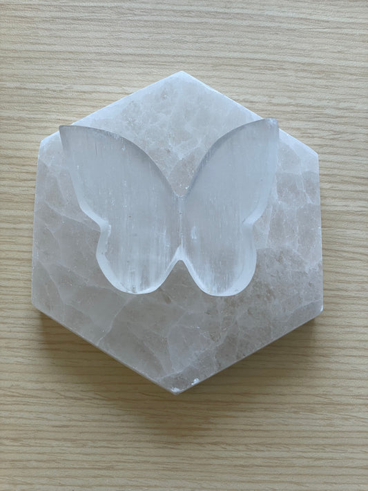 Selenite butterfly carving on hexagonal stone over wood surface