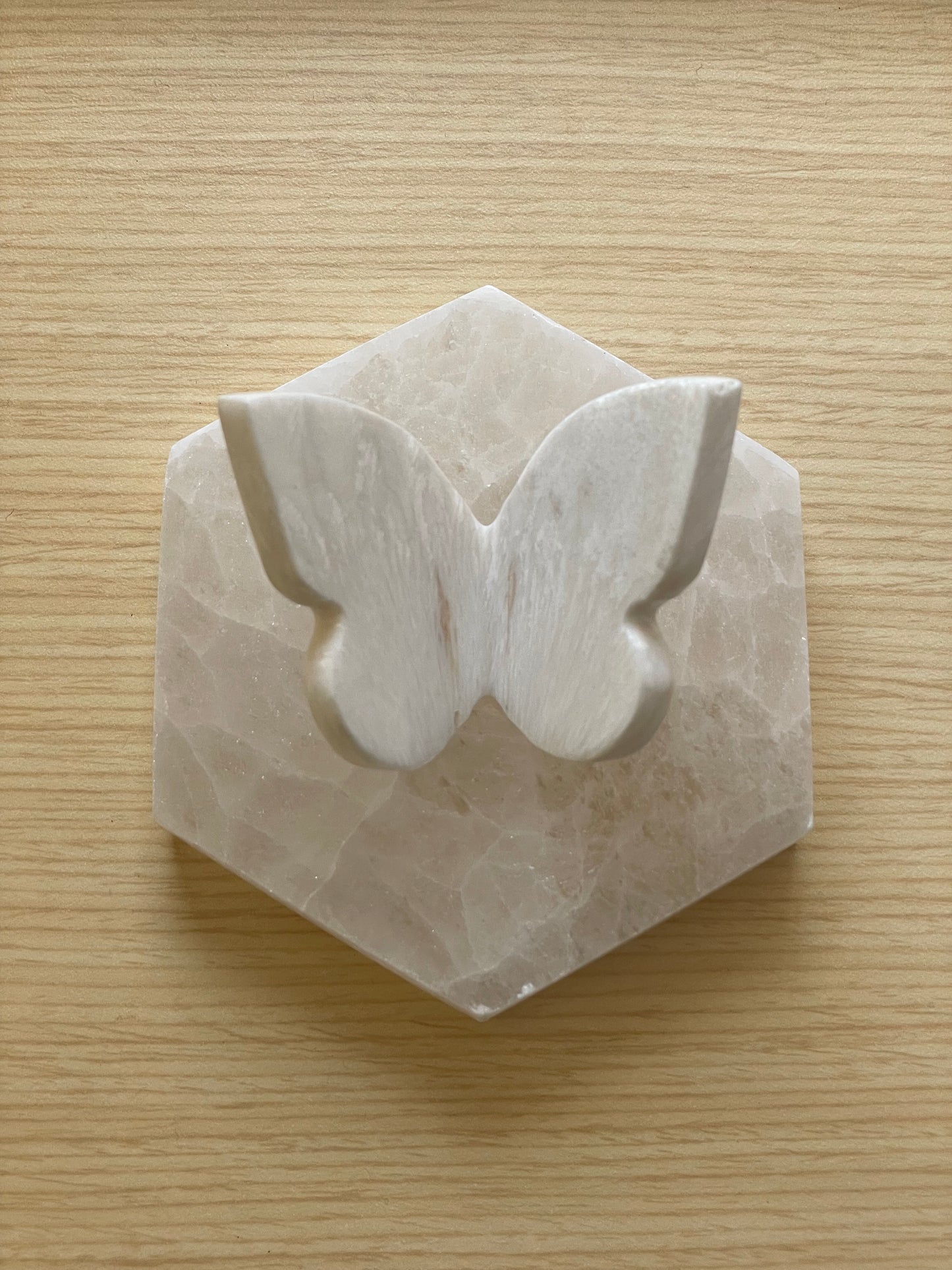 A polished white Scolecite butterfly shown on hexagon stone.