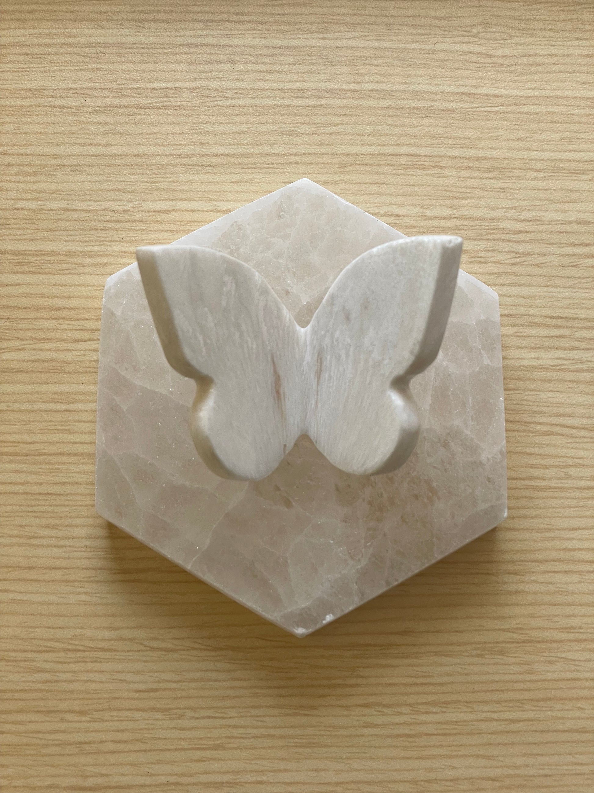 A polished white Scolecite butterfly shown on hexagon stone.