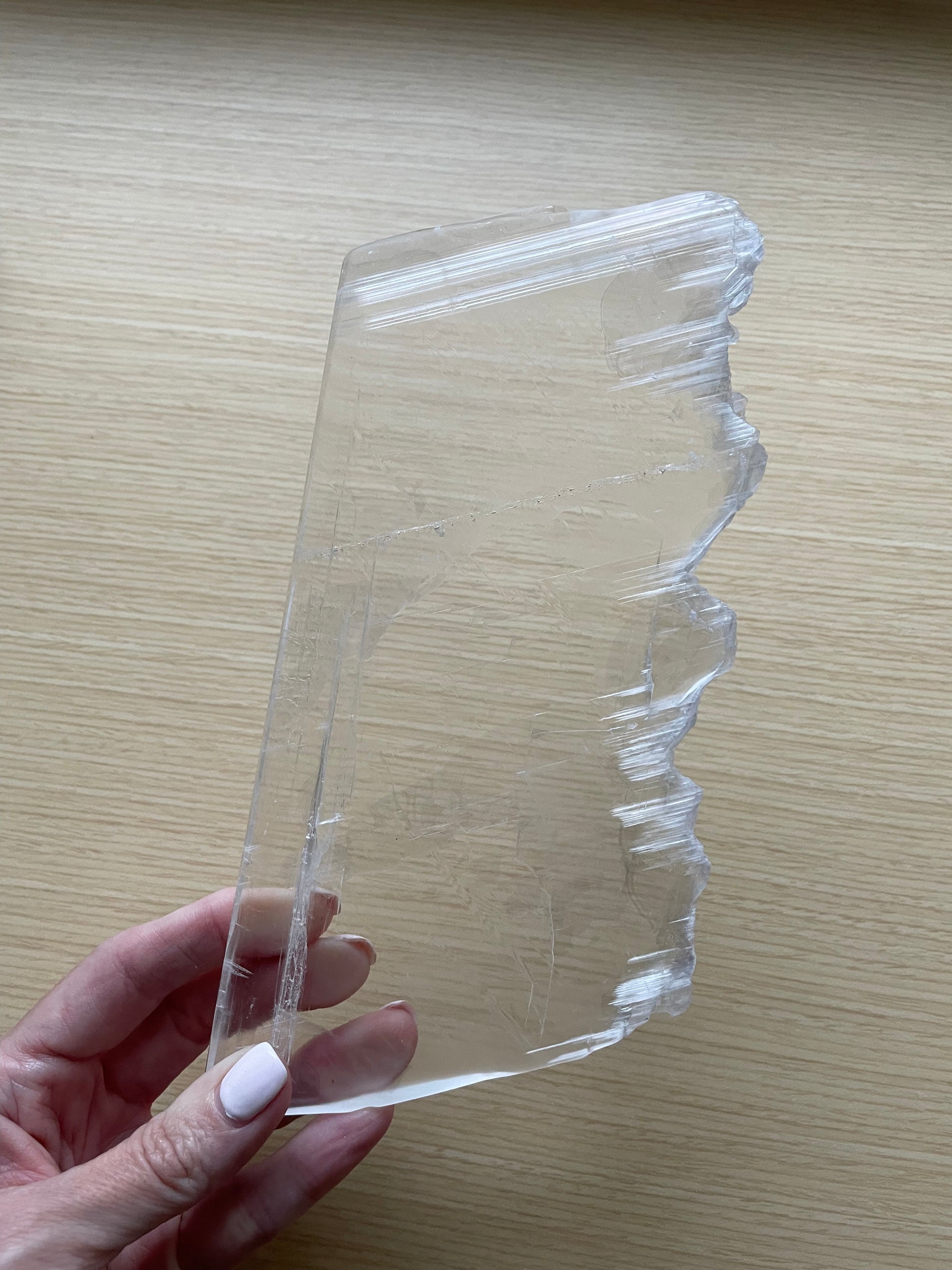 Selenite slab held by a hand on a wooden surface.