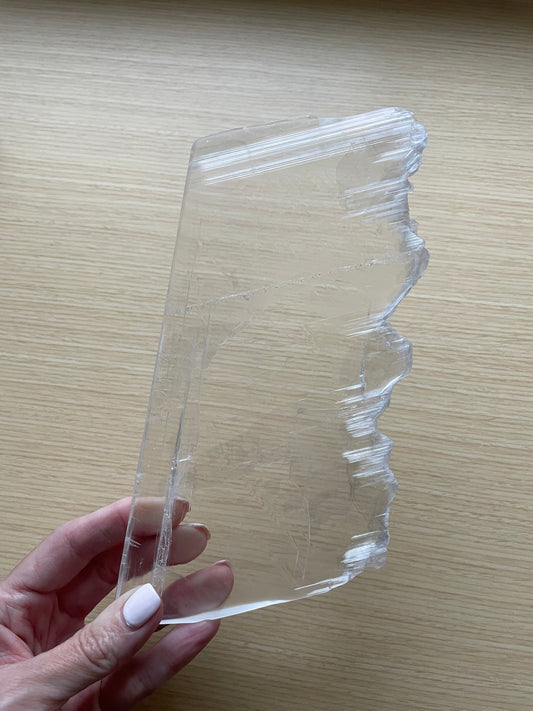 Selenite slab held by a hand on a wooden surface.