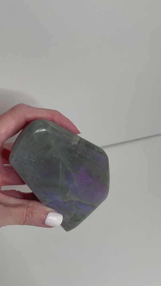 Labradorite freeform crystal showing vibrant reflections as a girl moves it in her hand.